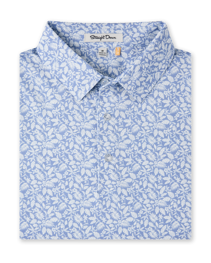 Close-up product view of the Tropics Lounge Polo in Blue Shade, featuring an allover white botanical print on a light blue background and a three-button placket.