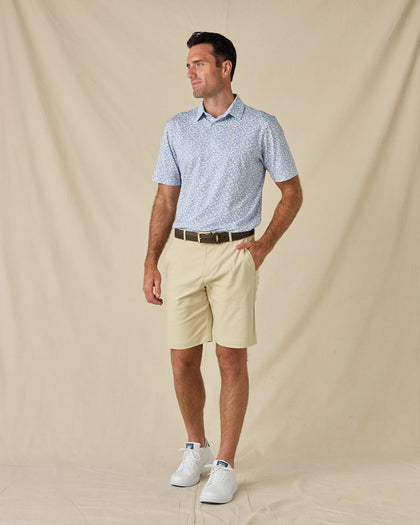 Model wearing the Tropics Lounge Polo in Blue Shade with khaki golf shorts, a brown belt, and white sneakers.