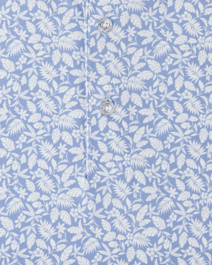 Detail view of the Tropics Lounge Polo in Blue Shade, highlighting the white botanical pattern, light blue fabric, and branded buttons.