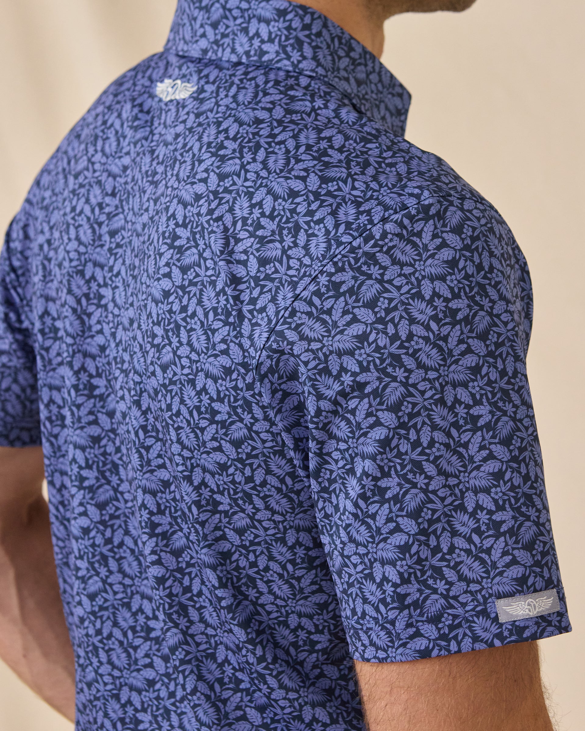 Side detail of the Tropics Lounge Polo in Tidal Blue showing the allover tropical pattern and Straight Down sleeve wings logo