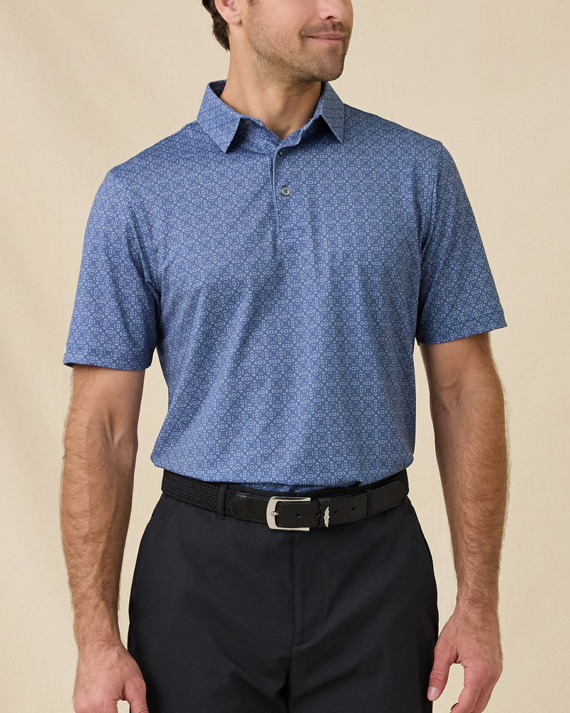 Model wearing the Sarasota Polo in Moonlight with an all-over geometric print, paired with dark pants and a black belt.