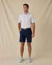 Model wearing the Pink Flamingo Polo in Sea Shell with navy golf shorts, a coordinating belt, and gray sneakers.