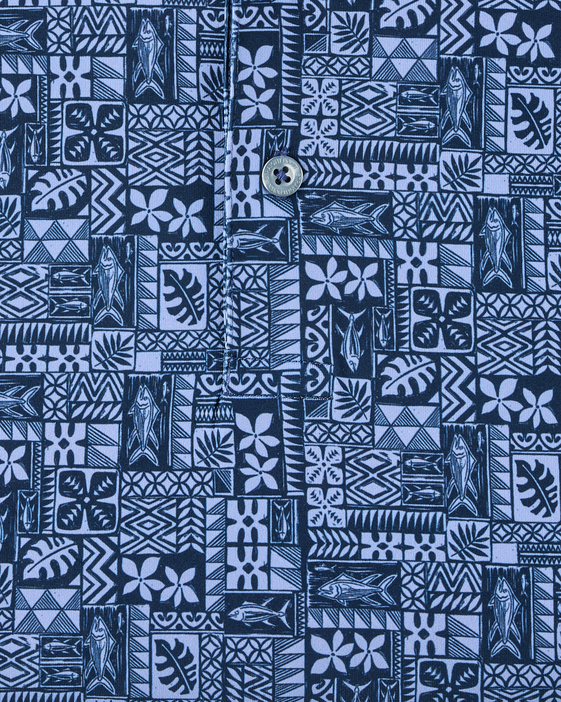 Close-up of the Reef Runner Polo in Blue Shade, highlighting the detailed fish, floral, leaf, and geometric motifs with branded button detail.