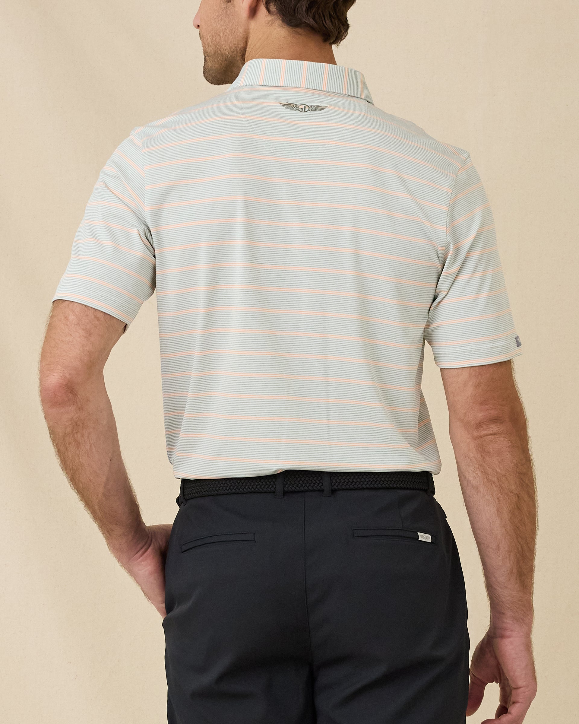 Back view of model wearing the Oceano Dunes Striped Polo in Cantaloupe, showing the horizontal stripe pattern and embroidered logo below the collar.
