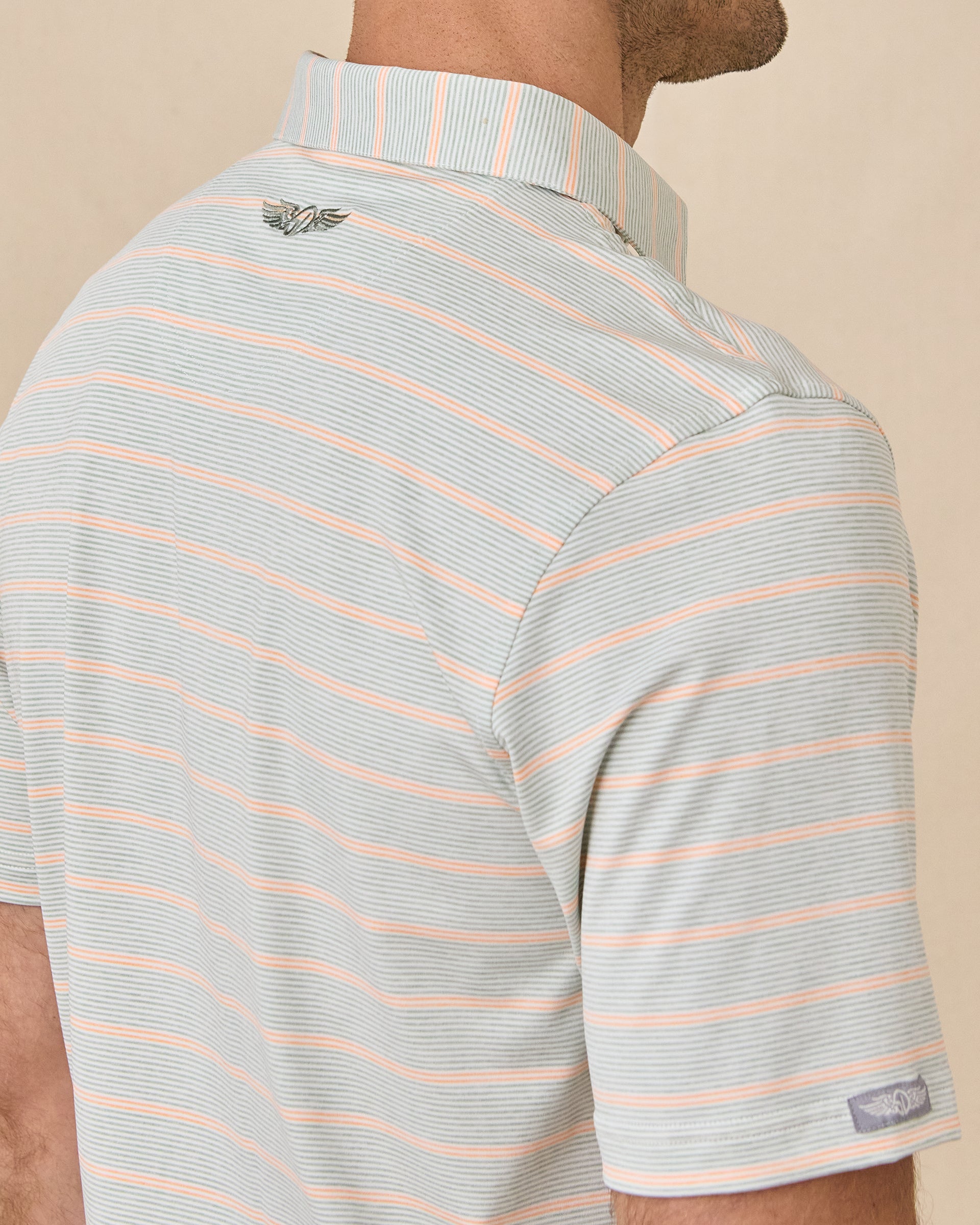 Close-up back view of the Oceano Dunes Striped Polo in Cantaloupe showing the striped collar, embroidered logo, and sleeve logo patch.