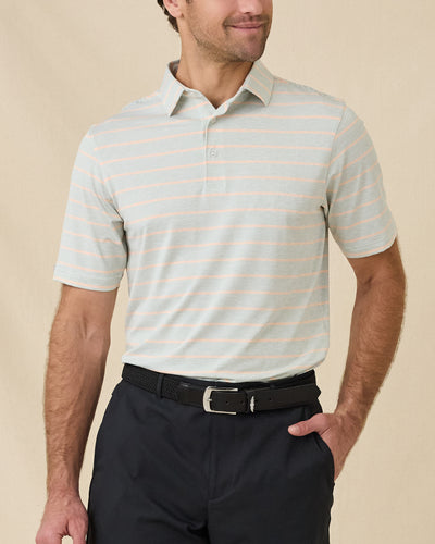 Model wearing the Oceano Dunes Striped Polo in Cantaloupe with black pants, showing the fine horizontal stripe pattern and classic polo collar.