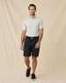 Full-length view of model wearing the Oceano Dunes Striped Polo in Cantaloupe with black shorts, a black belt, and black sneakers.