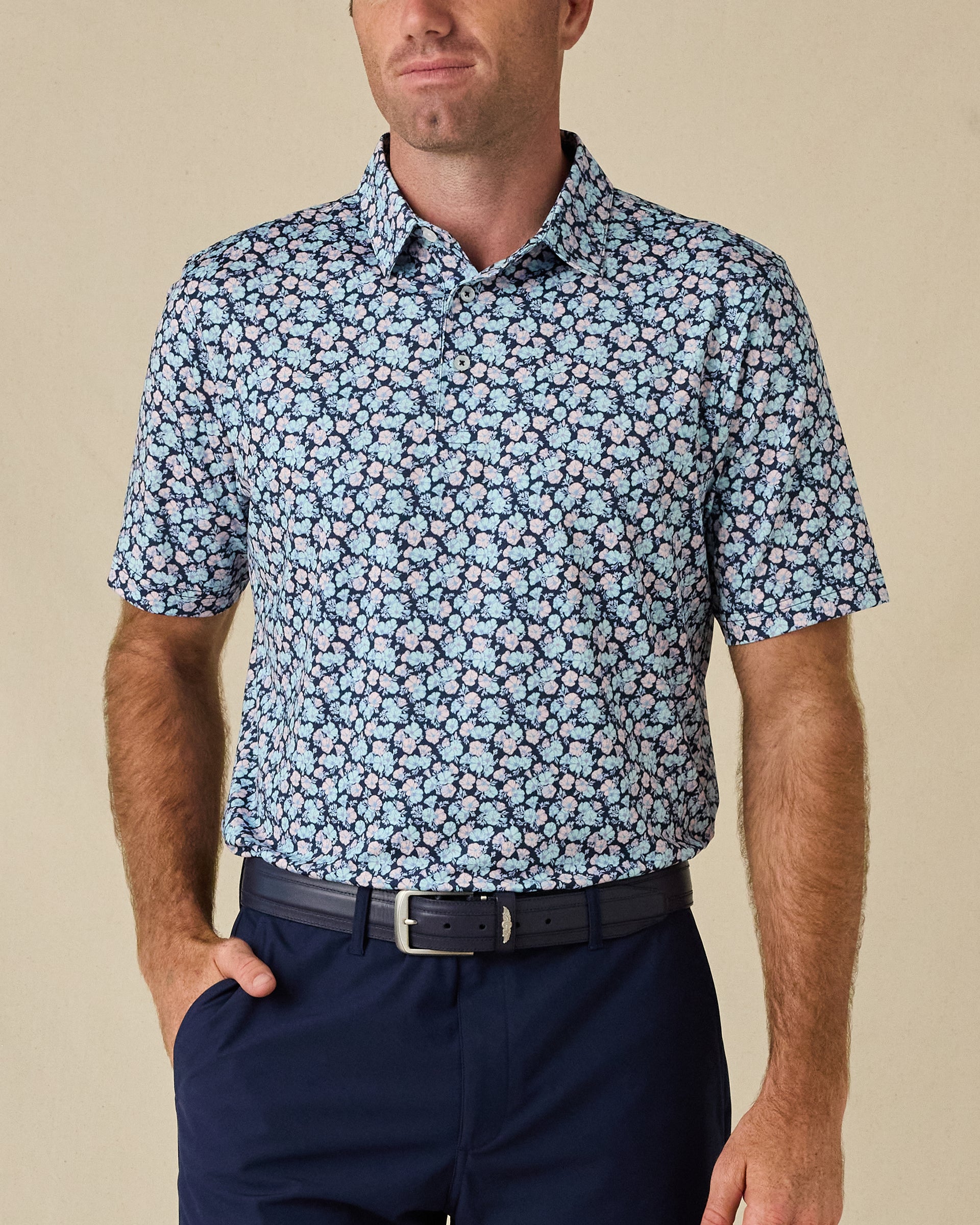 Model wearing the Point Reyes Polo in Mint Tea, featuring a dense floral print in light blue and soft pink against a navy background.