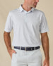 Model wearing the Trader Vics Polo in Blue Shade with an all-over light blue geometric print and light-colored golf shorts.