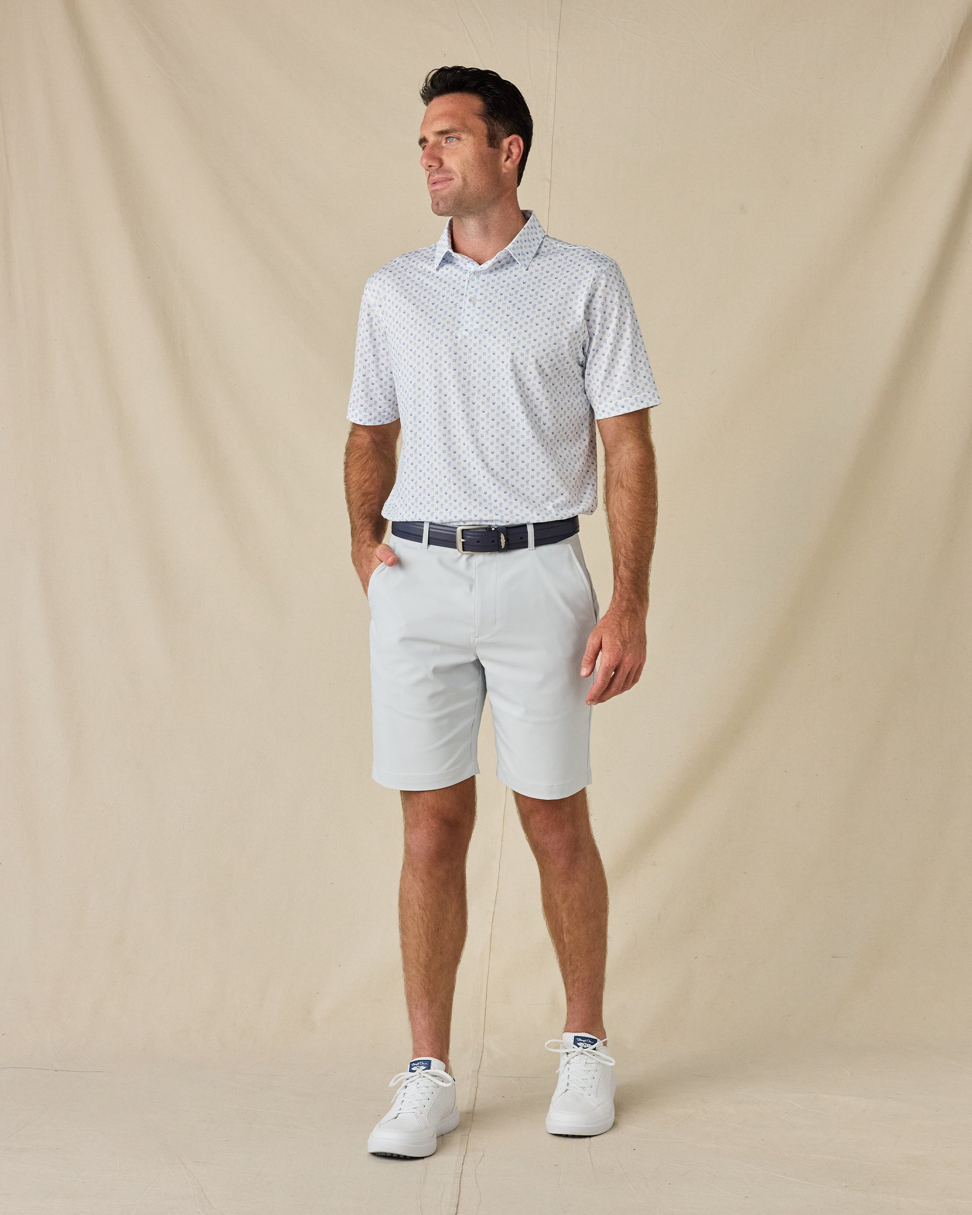 Model wearing the Trader Vics Polo in Blue Shade with light-colored golf shorts, a navy belt, and white sneakers.
