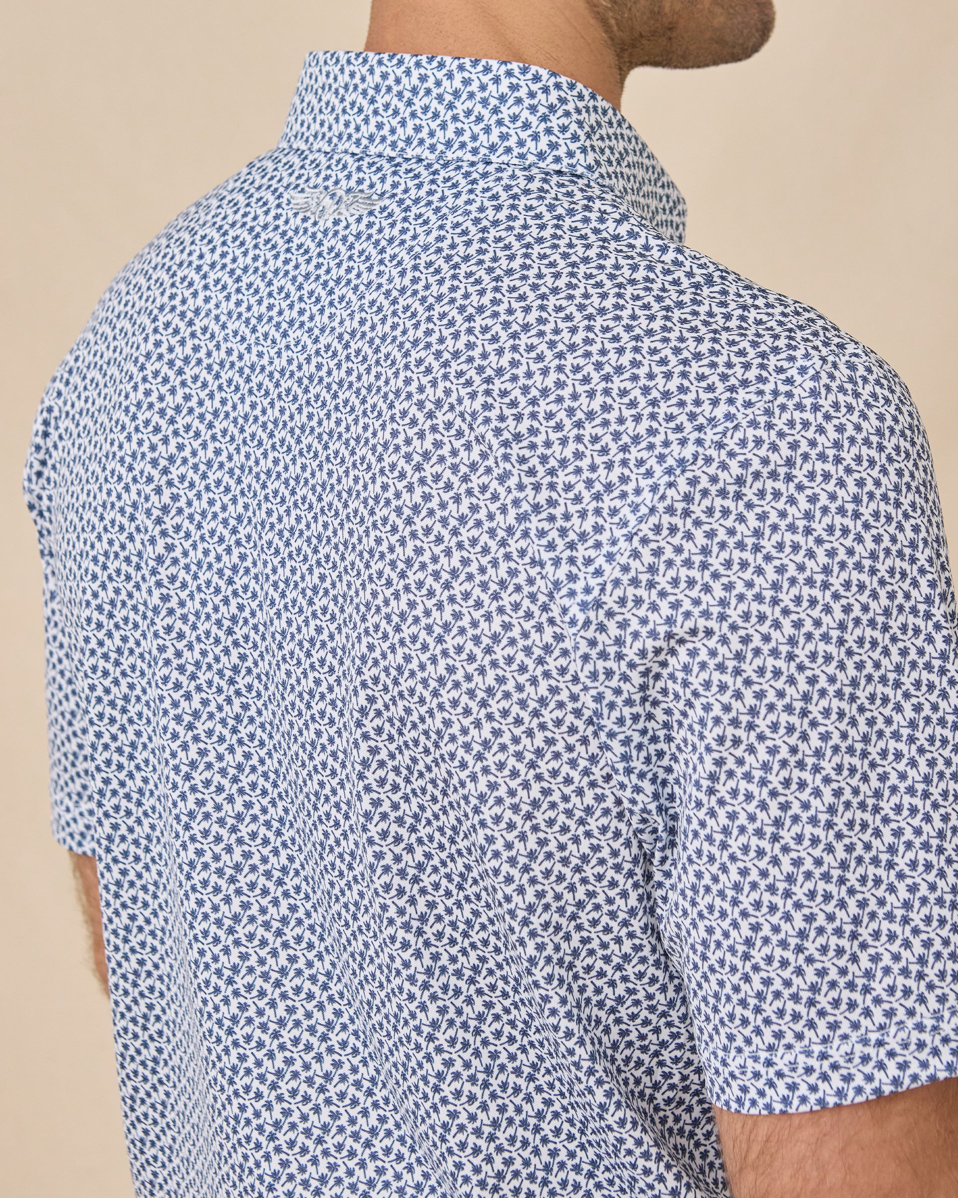 Back shoulder detail of the Date Palm Polo in New Indigo featuring a subtle embroidered Straight Down logo and allover palm tree print