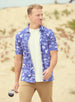 Islamorada Full Button Polo in Skipper, on model front view featuring a blue base with an all-over white nautical print of marlin, sailfish, coral, and palm trees, styled with khaki pants and worn open over a white tee on a golf course