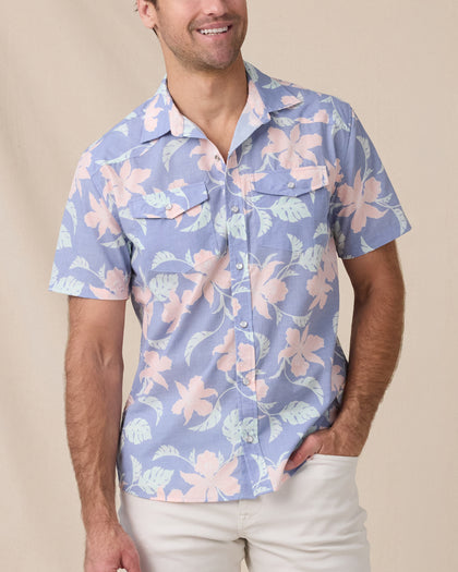 Man wearing a blue short-sleeve floral shirt with pink flowers, pearl snaps and dual chest pockets.