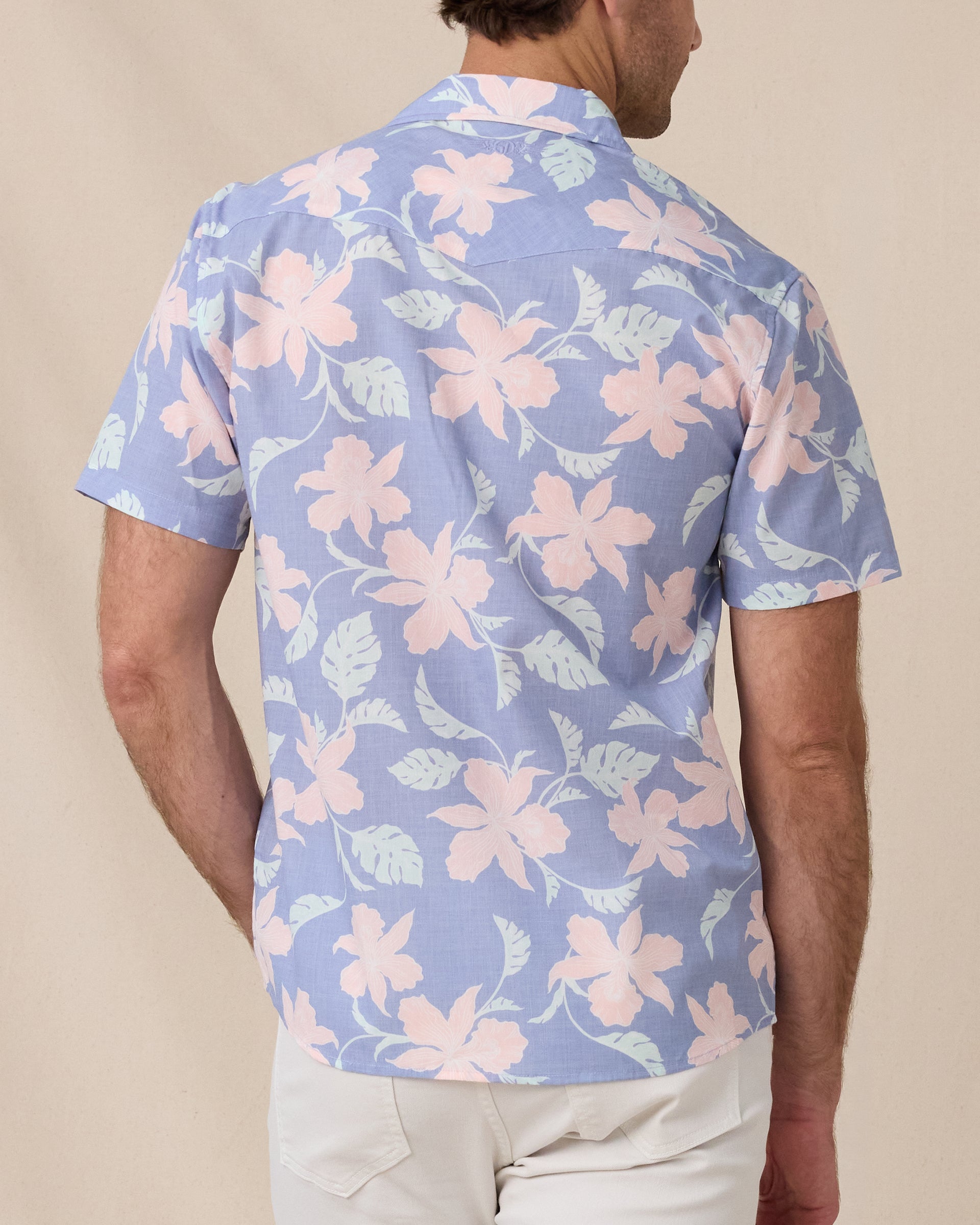 Back view of a man wearing a blue short-sleeve shirt with a pink and mint floral print.