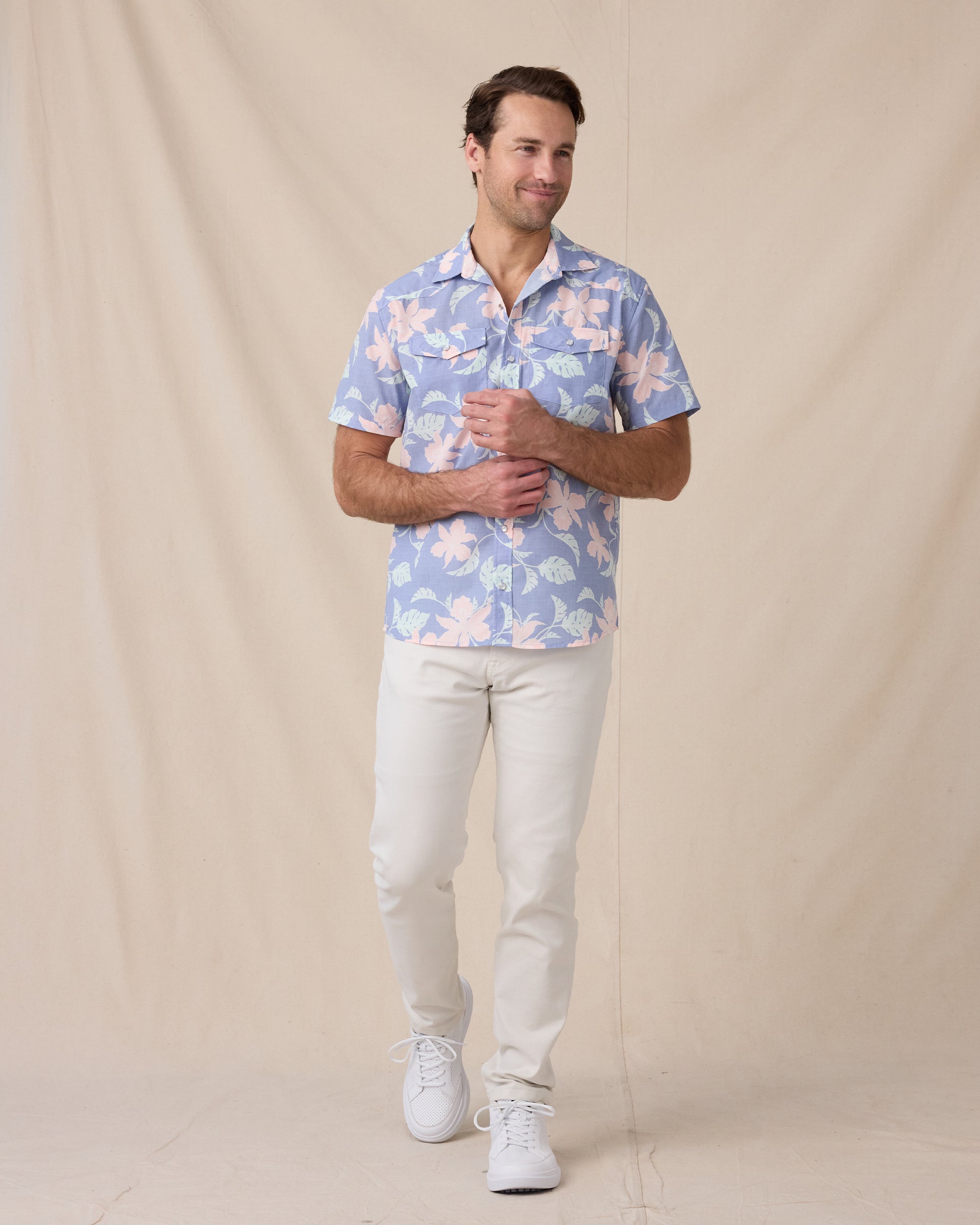 Man wearing a blue floral short-sleeve shirt with off-white pants and white sneakers.