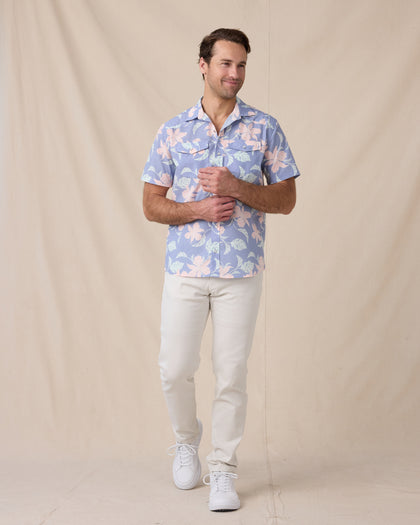 Man wearing a blue floral short-sleeve shirt with off-white pants and white sneakers.