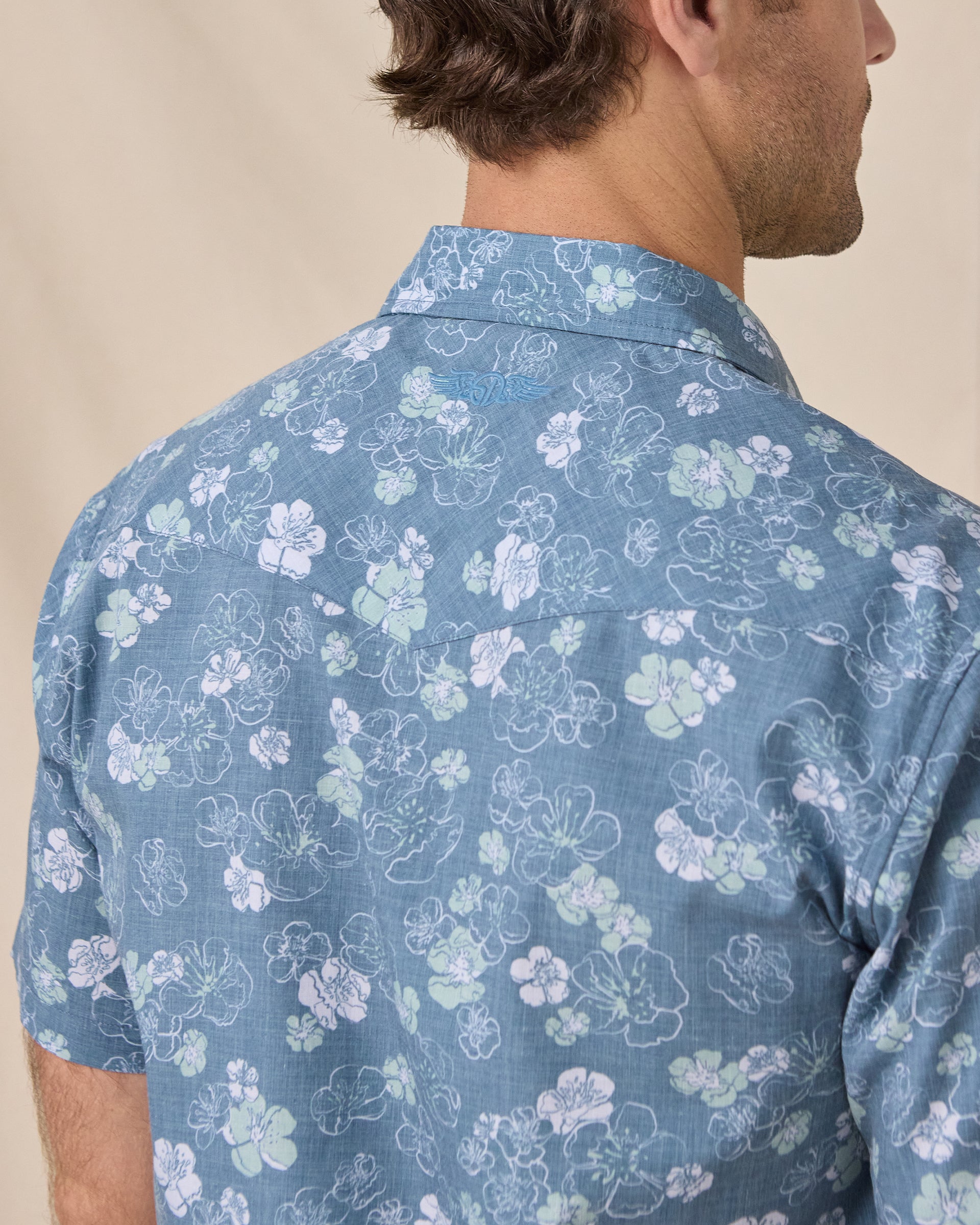 Close-up of the Celadine Woven Shirt showing the floral print and embroidered logo below the back collar.