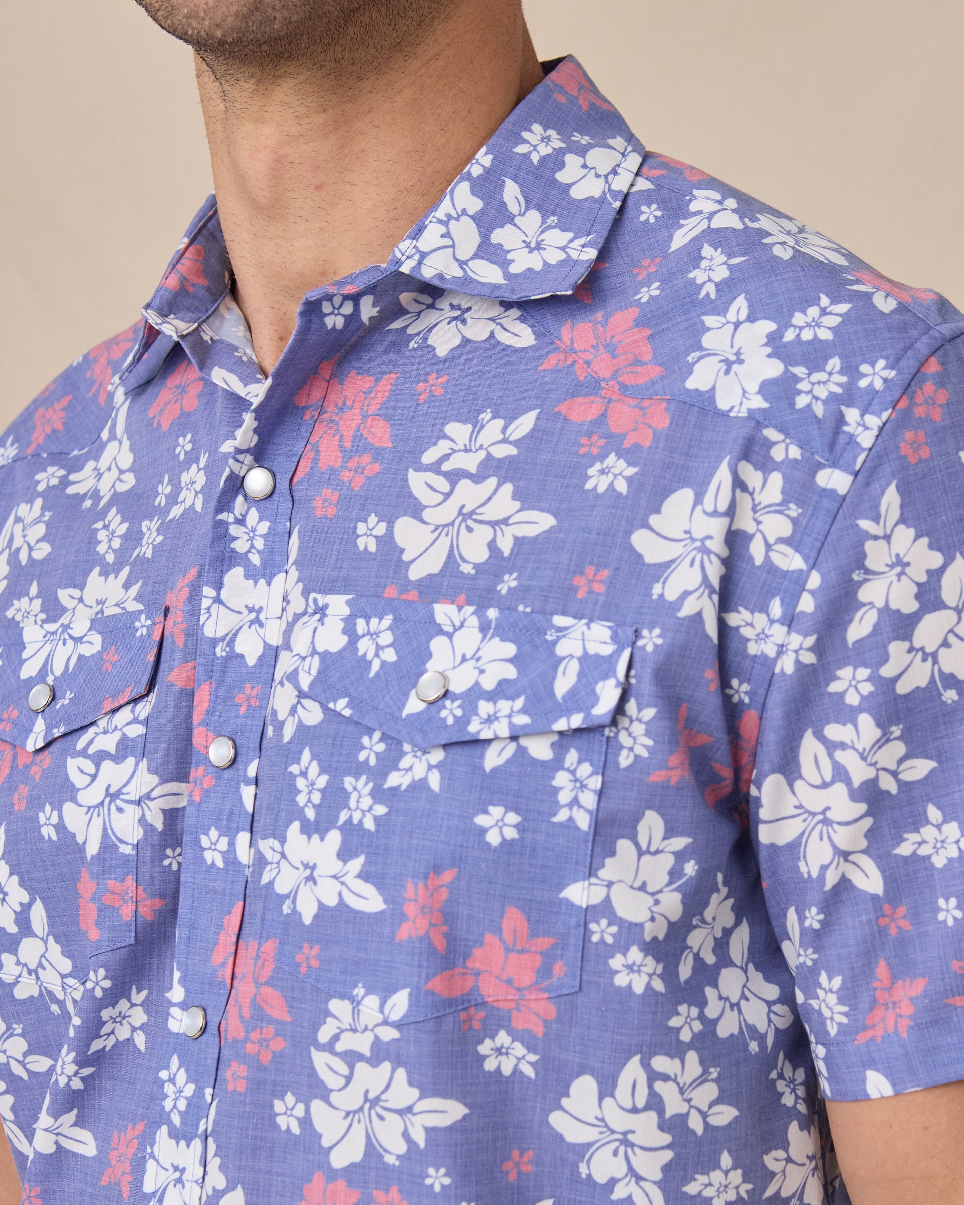 Close up of Paniolo Woven Shirt in Tidal Blue featuring a white and coral hibiscus floral print, pearl snap buttons, and dual chest pockets