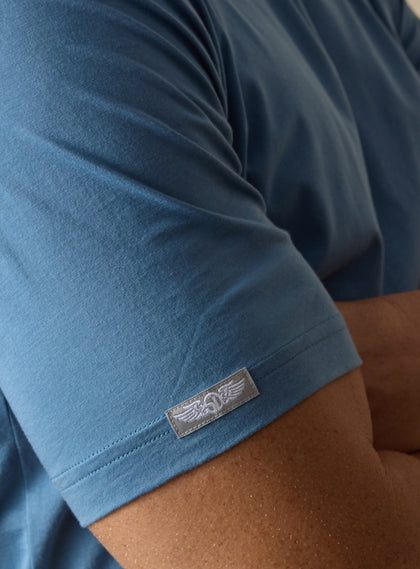 Men's Luxe Tee in Petrol, on model close up sleeve view featuring a medium blue short sleeve crew neck tee 