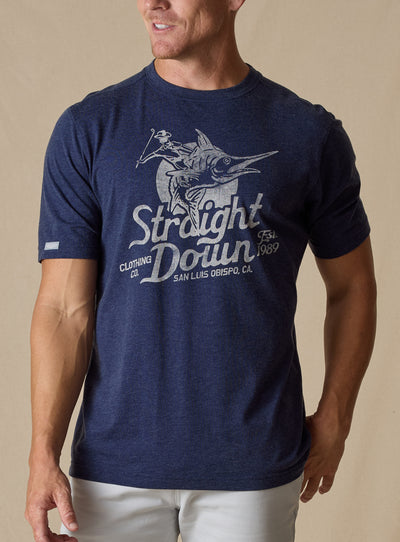 Marlin Rodeo Graphic Tee in New Indigo, front model view featuring a heathered navy short-sleeve crewneck tee with a vintage-style graphic of a golfer riding a leaping marlin, paired with light grey pants