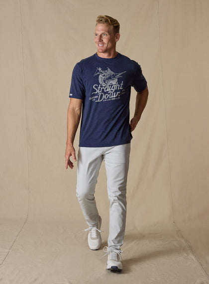 Marlin Rodeo Graphic Tee in New Indigo, full-length front model view featuring a heathered navy short-sleeve crewneck tee with a vintage-style graphic of a golfer riding a leaping marlin, paired with light grey pants and white shoes