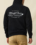 Men's Club Pro Hoodie in Black, back view on model featuring the large Straight Down Golf Company "Established 1989" graphic centered on the back, paired with tan pants