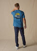 Vegas Vacation Graphic Tee in Petrol, full-length back model view featuring a heathered blue short-sleeve crewneck tee with a vintage-style graphic of a classic woody wagon loaded with golf clubs in front of a golden sun and retro roadside, paired with navy pants and white shoes