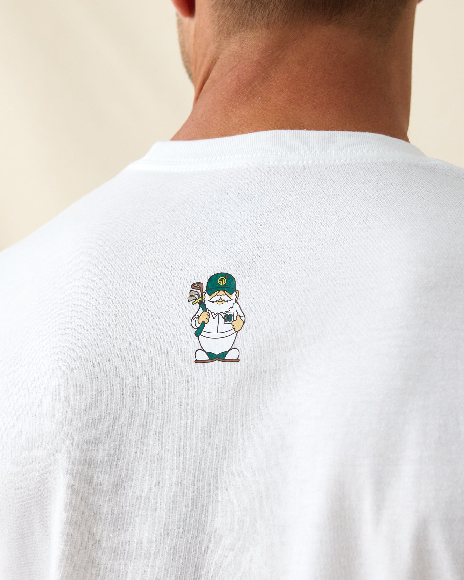 Men's IYKYK Tee in White, close-up back view on model highlighting the small golf gnome character graphic wearing a Straight Down logo cap and holding golf clubs at upper back