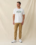Men's IYKYK Tee in White, full length front view on model featuring a white base with a four golf gnome character graphic and IYKYK text in green on the chest, paired with khaki pants and white shoes