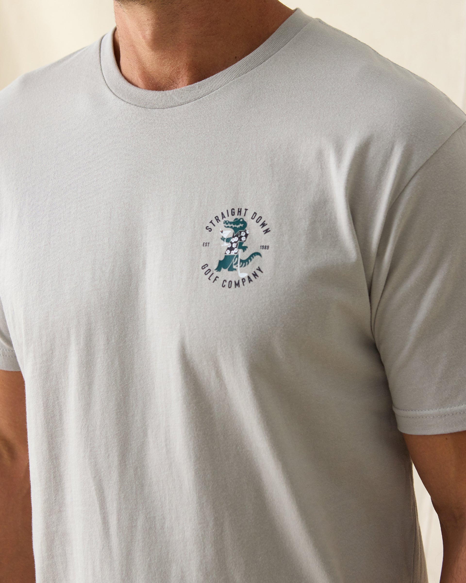 Men's Alligator Alley Tee in Light Grey, close-up model view featuring the Straight Down Golf Company Est. 1989 alligator graphic on the left chest