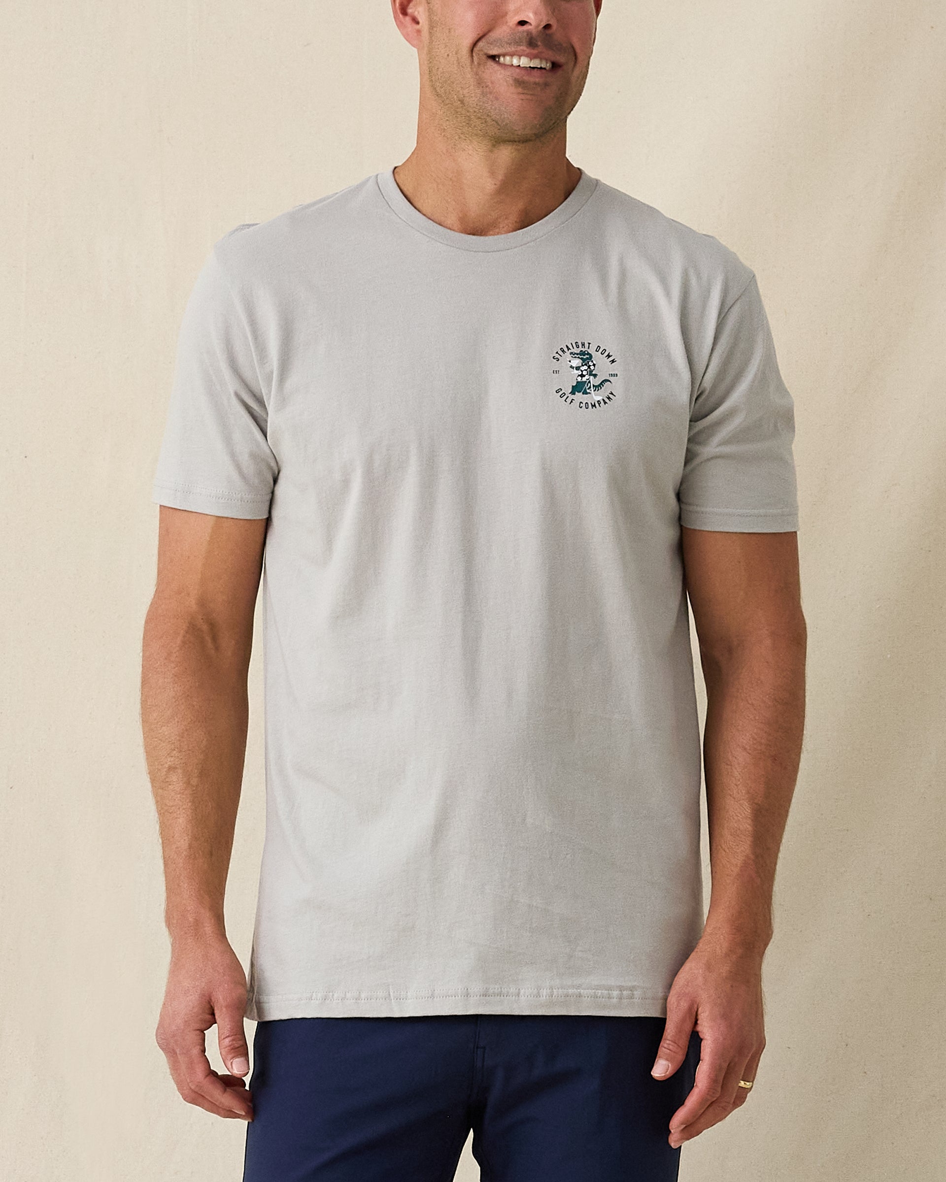 Men's Alligator Alley Tee in Light Grey, front model view featuring a light grey short sleeve crewneck tee with the Straight Down Golf Company Est. 1989 alligator graphic on the left chest paired with navy pants