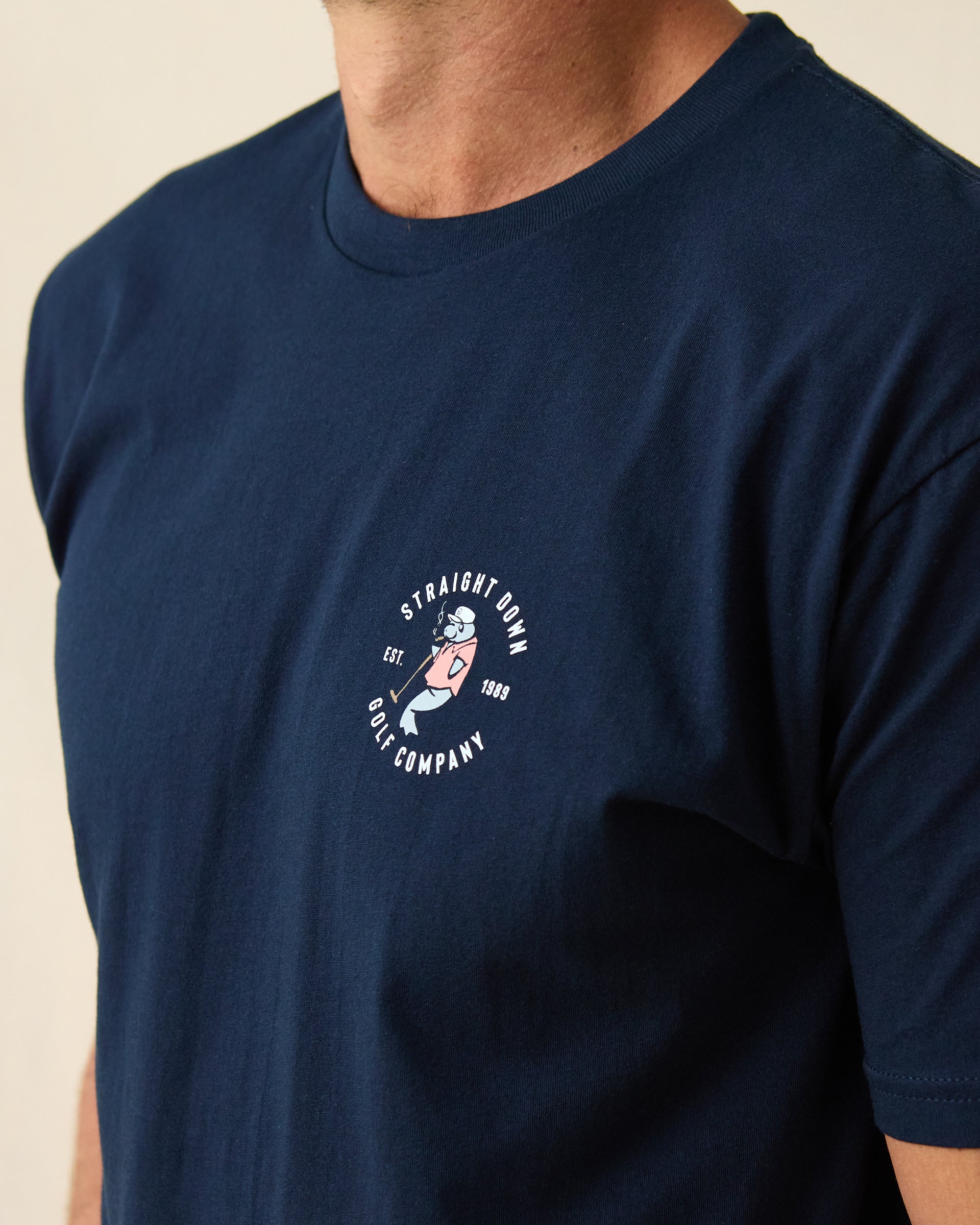 Men's Mana-Tee in Navy, close-up front view on model highlighting the circular Straight Down Golf Company Est. 1989 graphic with manatee character on left chest