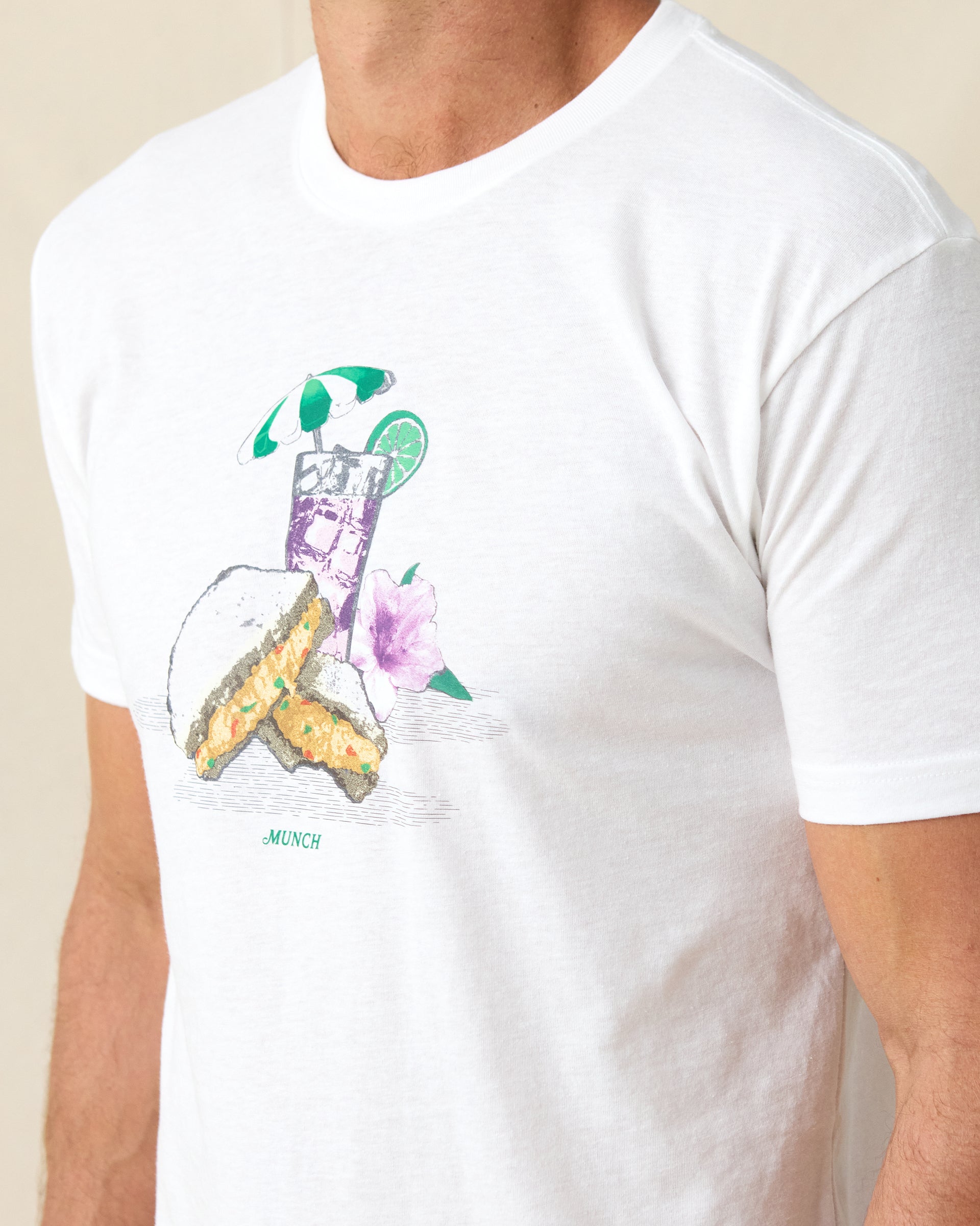 Men's Munch Tee in White, close-up front view on model highlighting the pimento cheese sandwich and iced drink graphic with MUNCH text on the chest