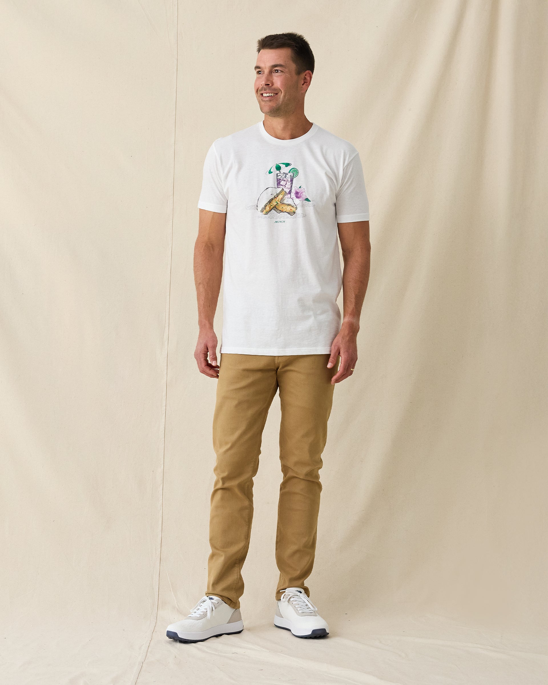 Men's Munch Tee in White, full length front view on model featuring a white base with a pimento cheese sandwich and iced drink graphic with MUNCH text on the chest, paired with khaki pants and white shoes