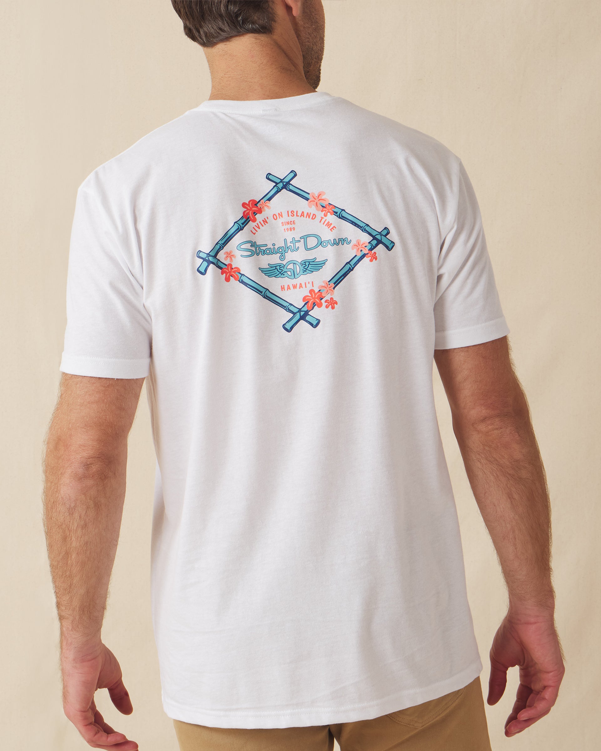 Men's Island Time Tee in White, back view on model featuring a Straight Down Livin' On Island Time Since 1989 Hawai'i graphic with a bamboo diamond frame and coral flowers in blue and coral