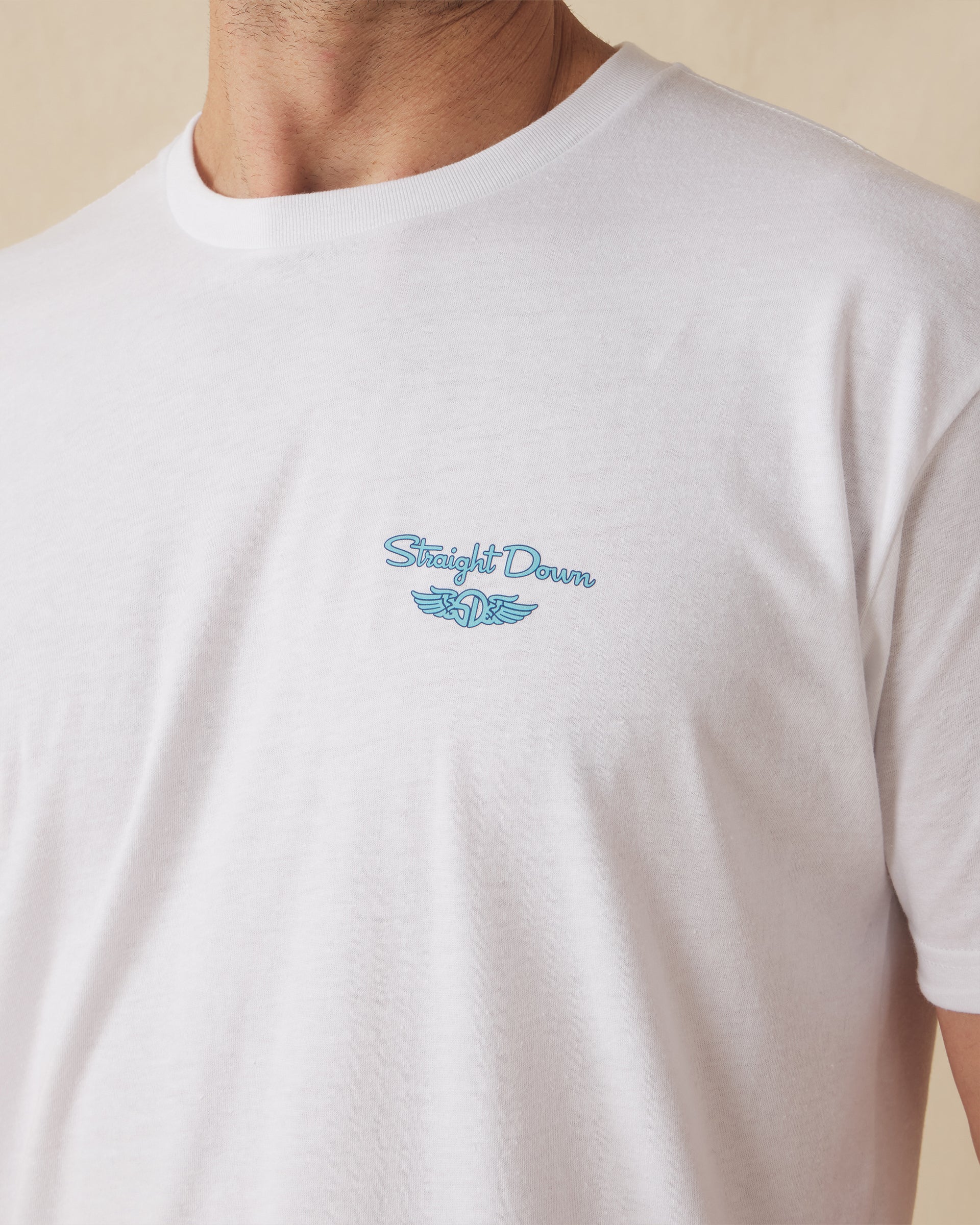 Men's Island Time Tee in White, close-up front detail view of the small blue Straight Down logo graphic on the left chest