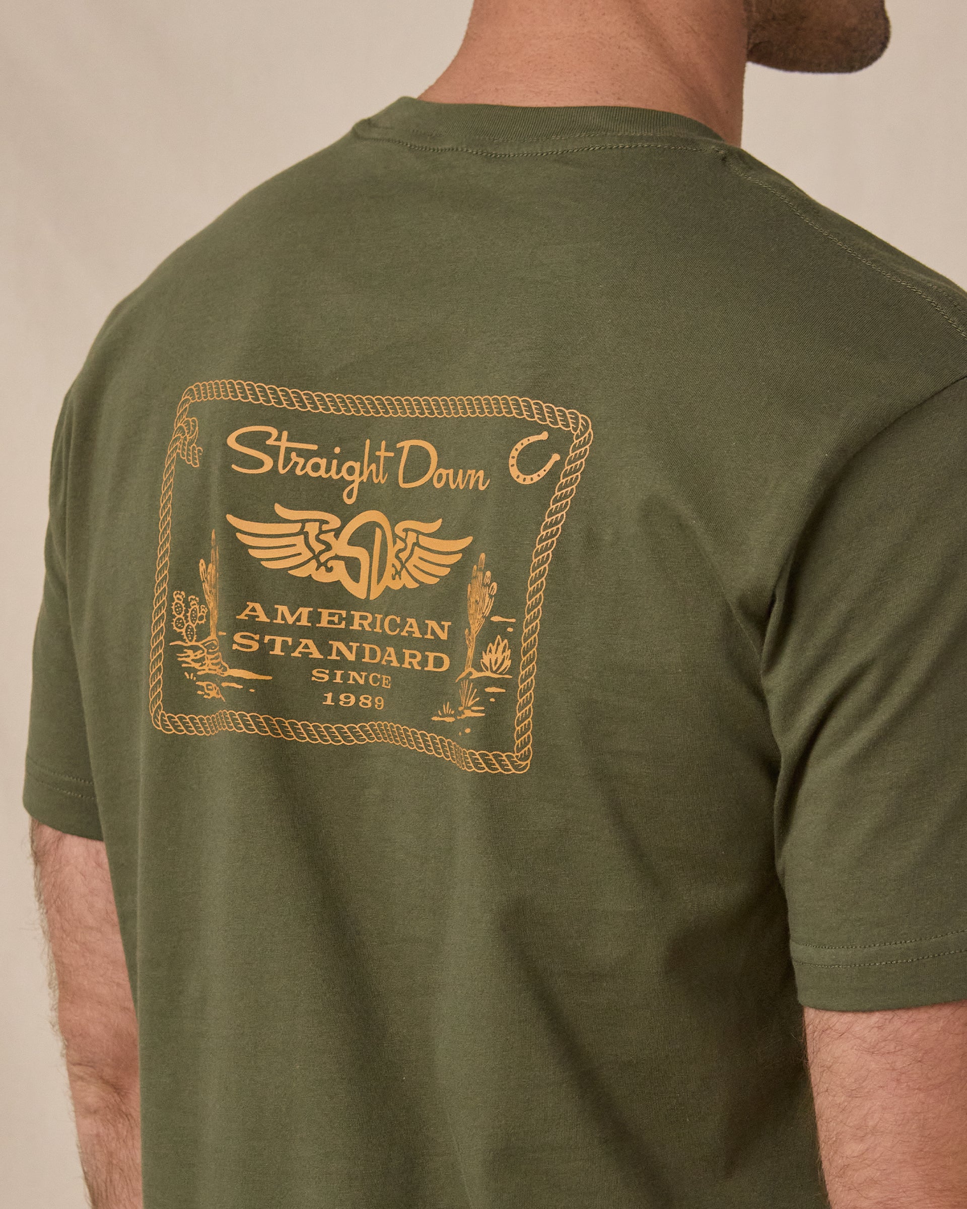 Close-up of the American Standard Tee in Army Green showing the large gold western-inspired Straight Down graphic across the upper back.