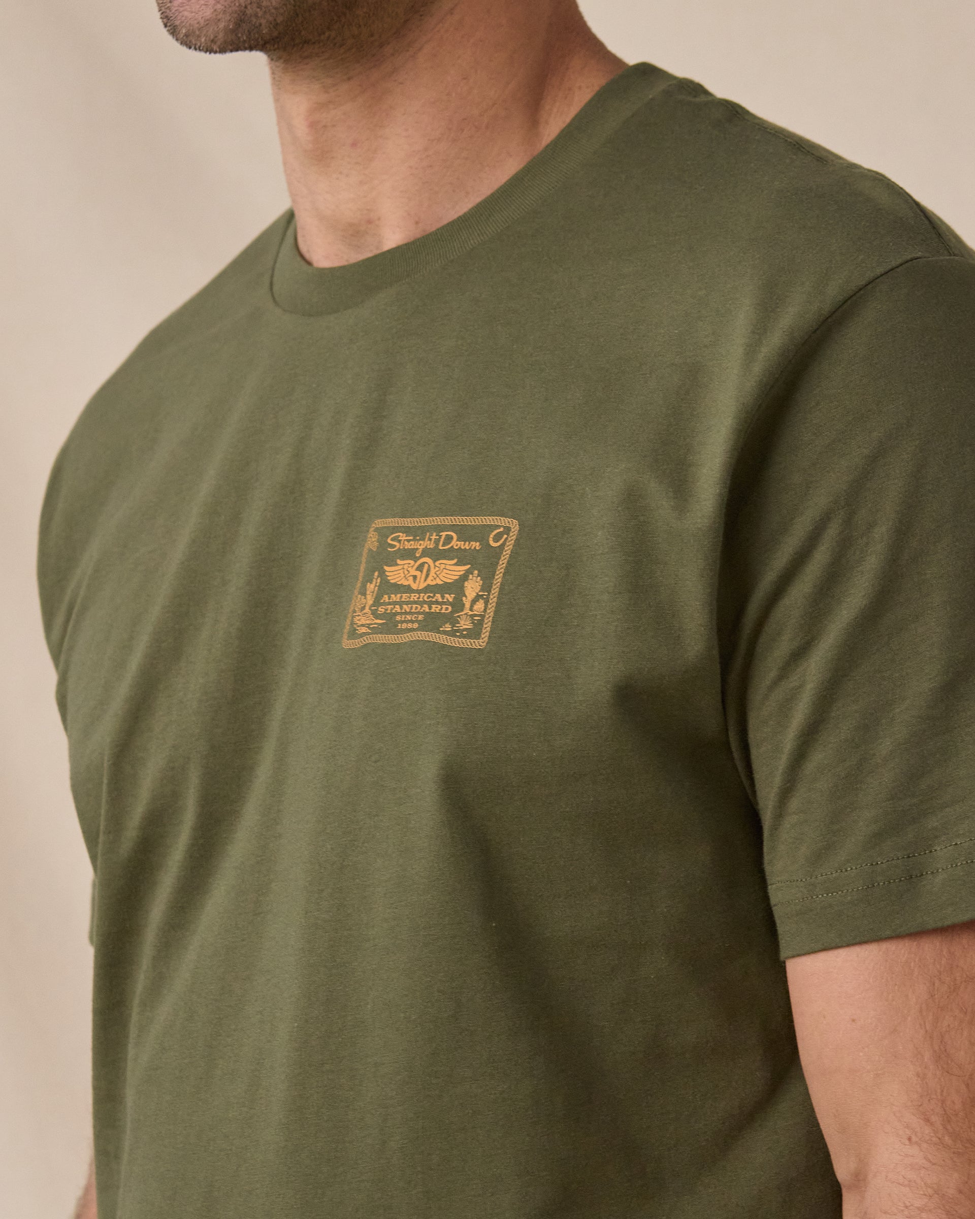 Close-up of the American Standard Tee in Army Green showing the small gold Straight Down American Standard graphic on the left chest.