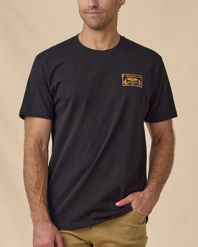 Man wearing the American Standard Tee in Black with a small gold graphic on the left chest.