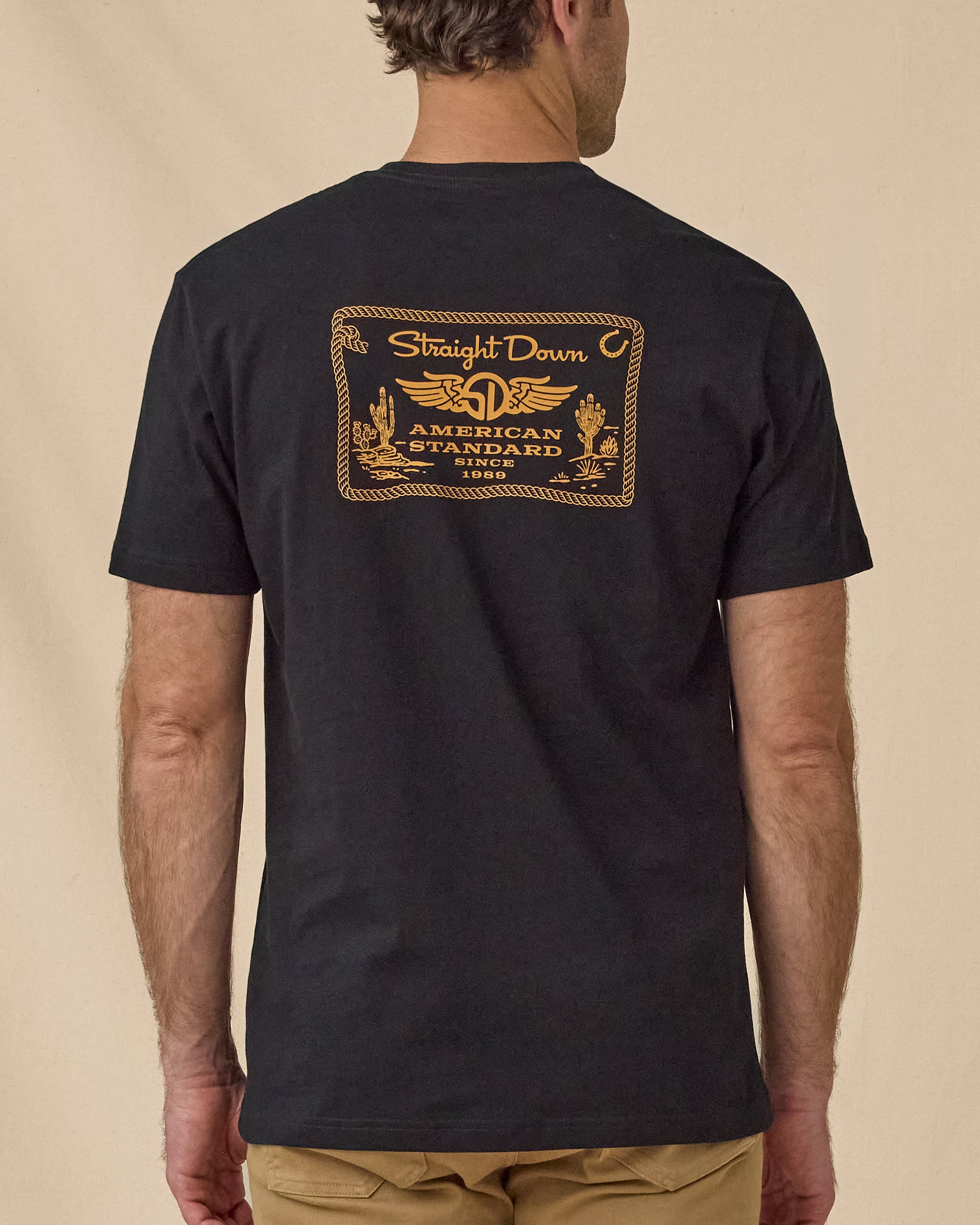 Back view of the American Standard Tee in Black featuring a large gold Straight Down American Standard 