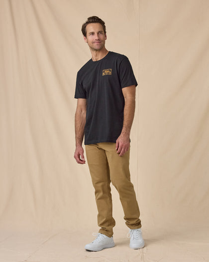Man wearing the American Standard Tee in Black with tan pants and black sneakers.