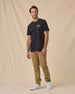 Man wearing the American Standard Tee in Black with tan pants and black sneakers.