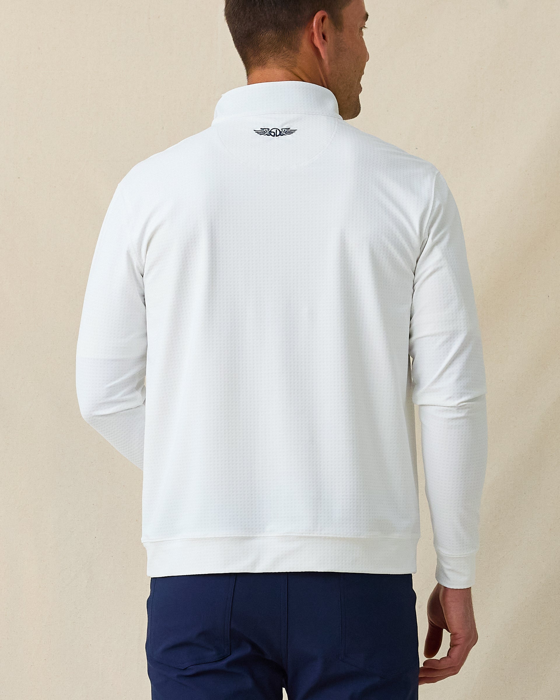 Back view of men’s white textured quarter-zip pullover with subtle embroidered logo at the neck, paired with navy pants.