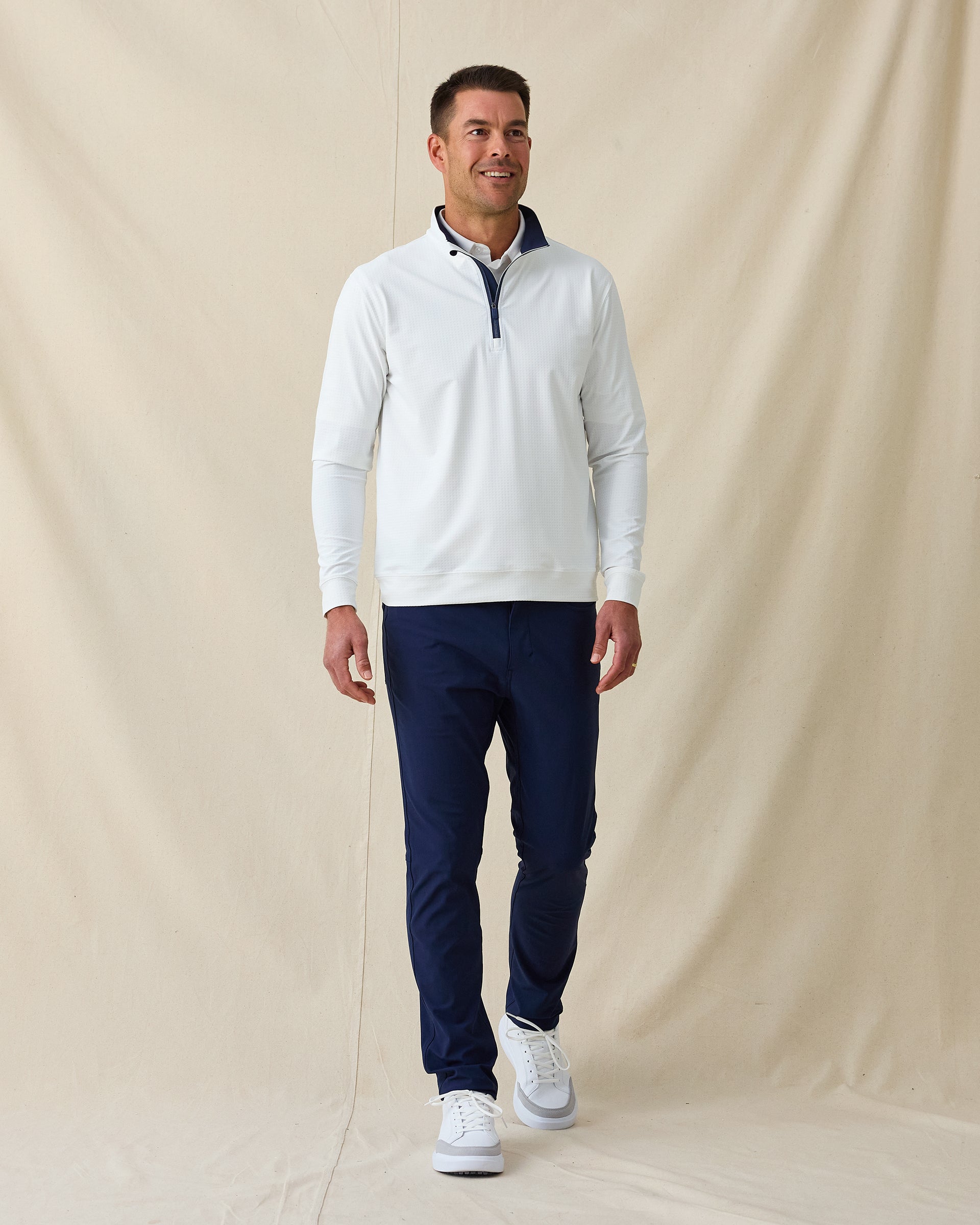 Men’s white quarter-zip pullover styled with navy pants and white sneakers in a clean golf outfit.