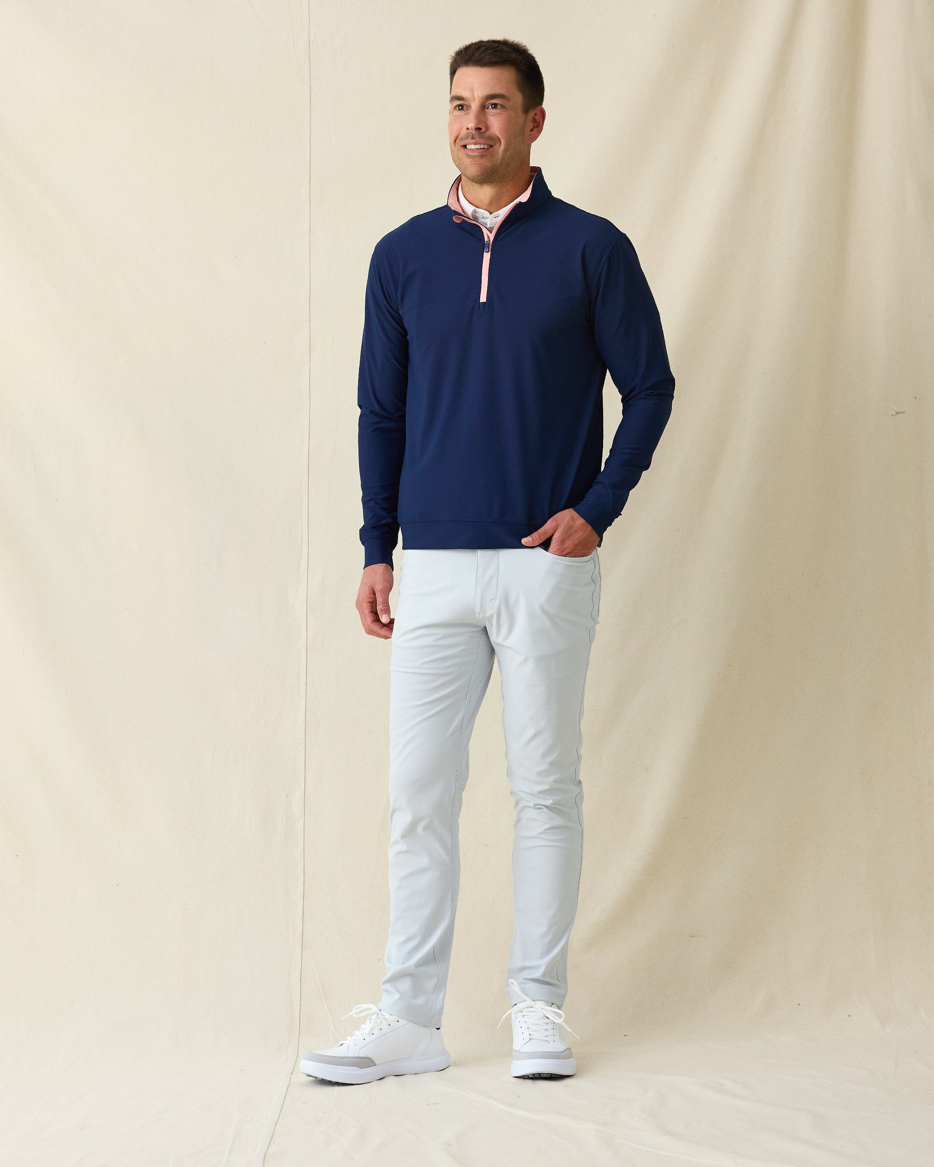 Men's Bel Air Quarter Zip in New Indigo, full length model view featuring a navy long sleeve quarter zip pullover with a subtle textured fabric and pink contrast zip placket, layered over a white striped polo, styled with light gray pants and white shoes