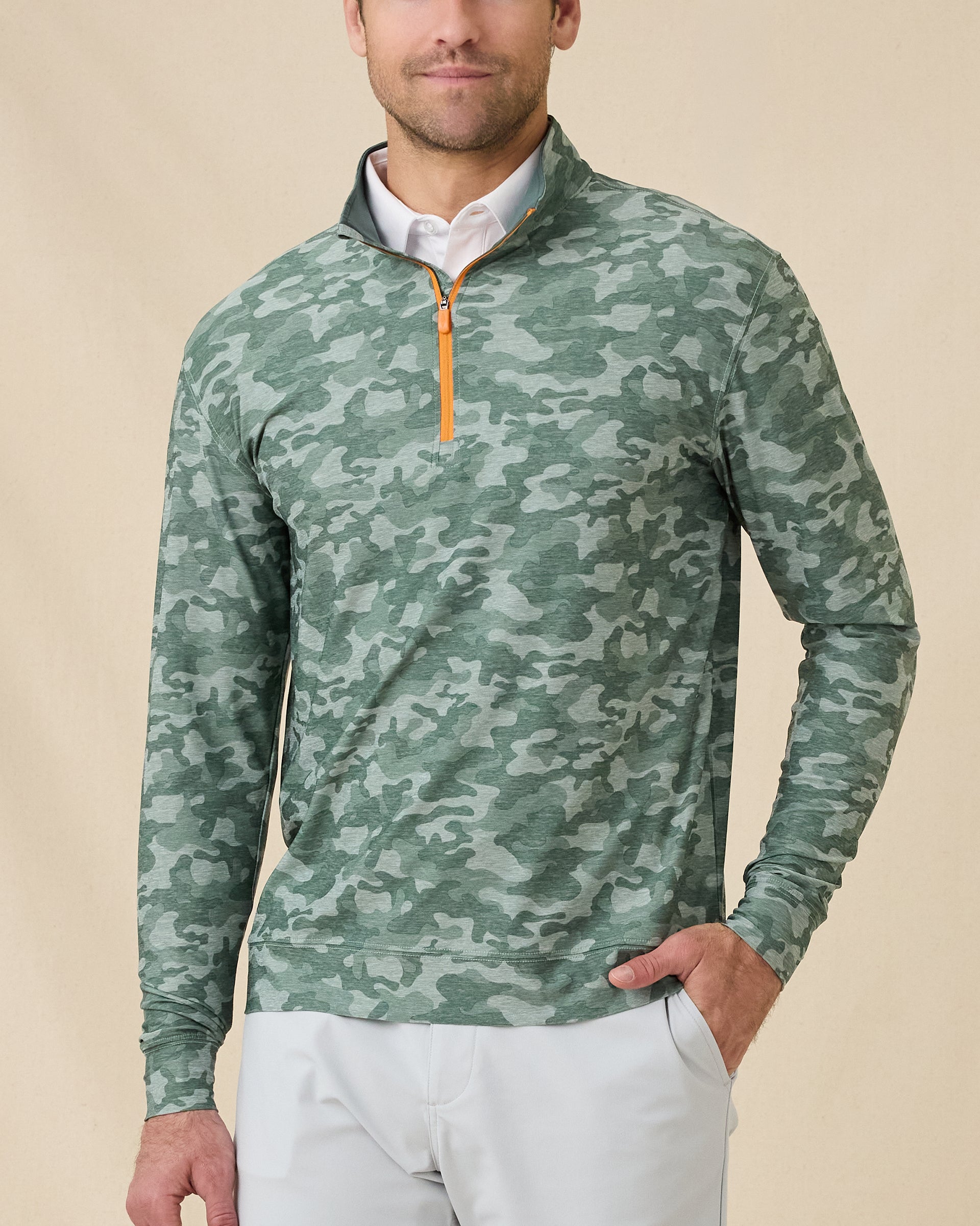Model wearing the Arlington Quarter Zip in Dark Forest over a white polo, featuring a green camouflage print and orange zipper.