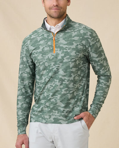 Model wearing the Arlington Quarter Zip in Dark Forest over a white polo, featuring a green camouflage print and orange zipper.