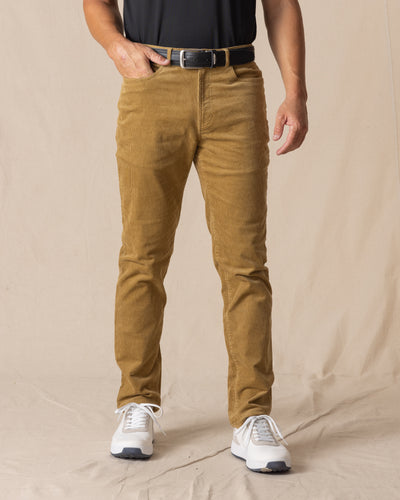Men's Smithson Corduroy Pant in Bronze, front on-model view featuring a golden tan corduroy fabric, black leather belt, and white shoes