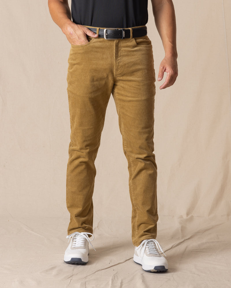 Men's Smithson Corduroy Pant in Bronze, front on-model view featuring a golden tan corduroy fabric, black leather belt, and white shoes