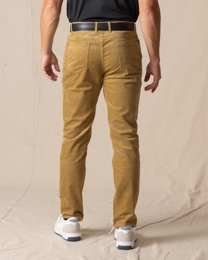 Men's Smithson Corduroy Pant in Bronze, back on-model view featuring a golden tan corduroy, styled with a black t-shirt, black leather belt, and white shoes